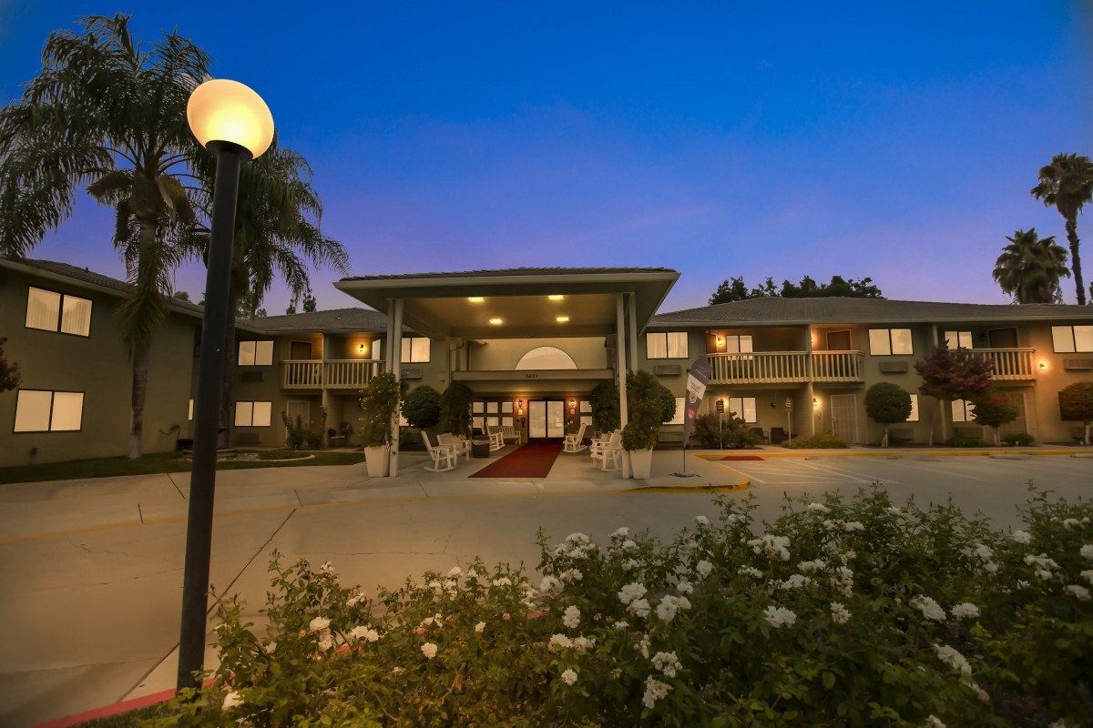 A well-lit hotel entrance at night, surrounded by lush landscaping.