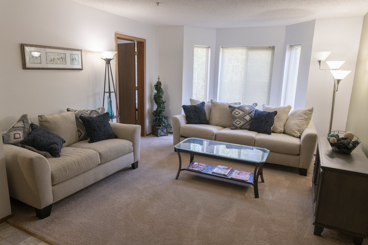 A cozy living room featuring two beige sofas, a glass coffee table, and a floor lamp.