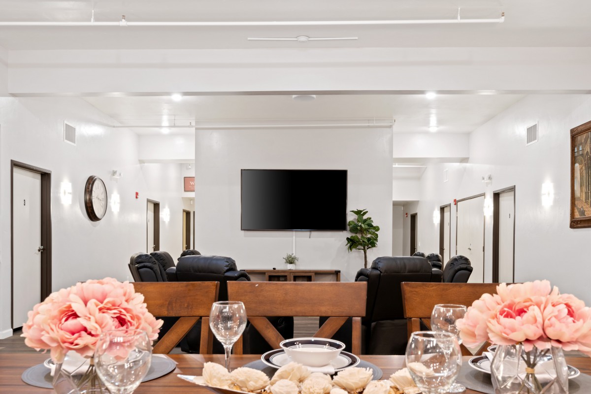 A modern living room features a dining setup with elegant place settings and floral decor, centered around a television and comfortable seating.