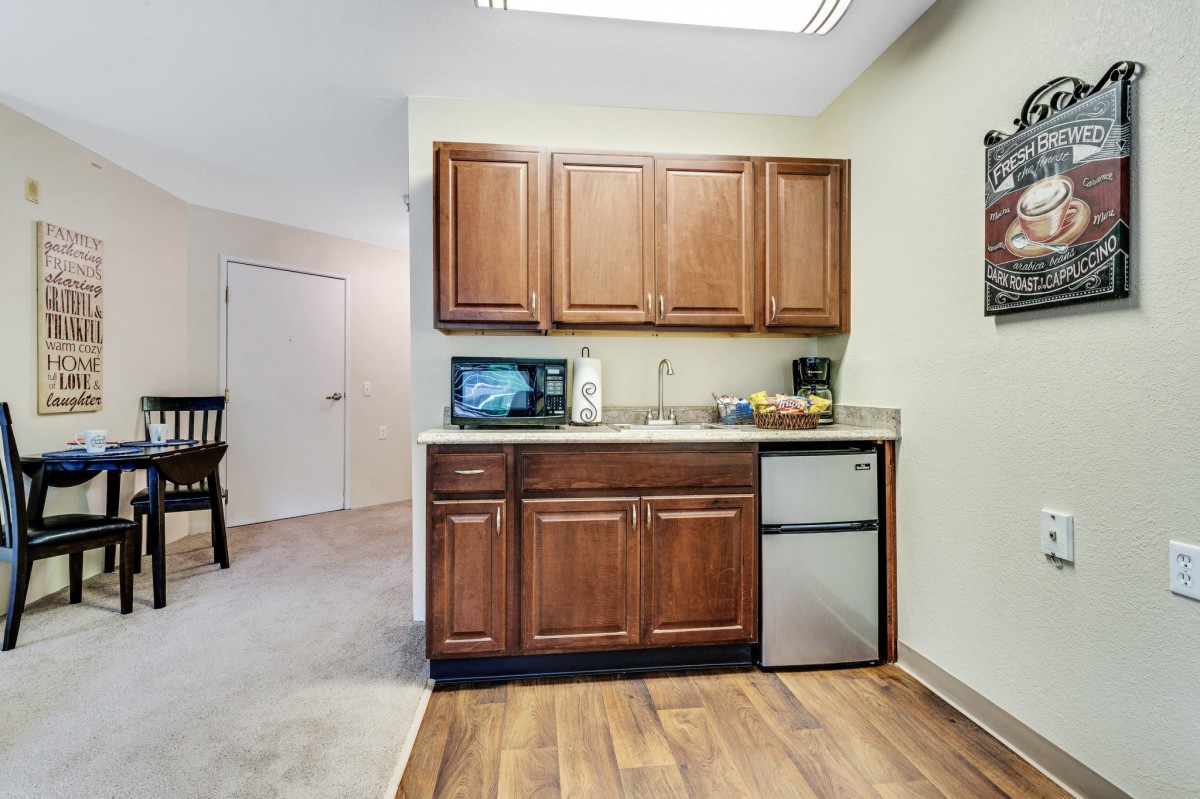 A small kitchenette area with wooden cabinets, a mini fridge, microwave, and sink.