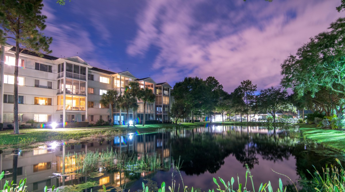 A serene nighttime scene with a building reflecting on a calm lake under a cloudy sky.