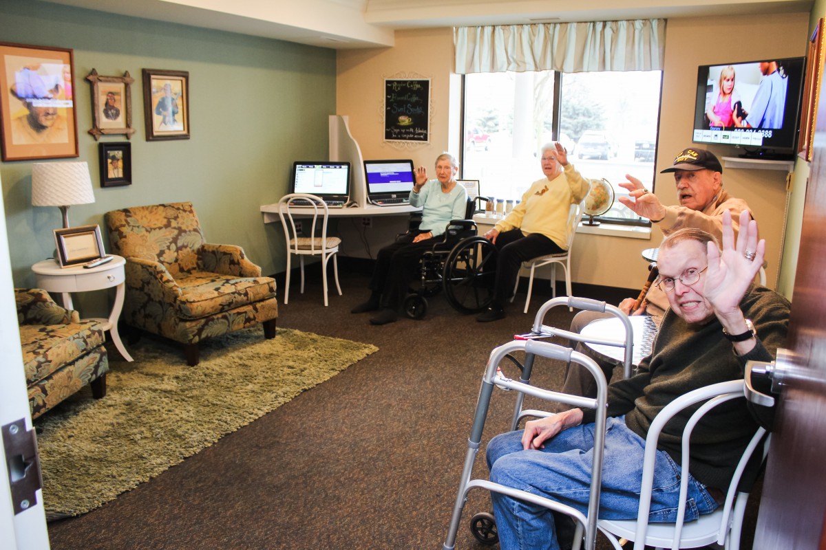 A group of seniors relax and socialize in a community room equipped with computers.