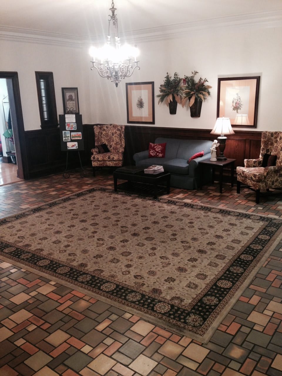 A cozy living room with a sofa, chairs, and a rug, accented by decorative artwork and a table lamp.
