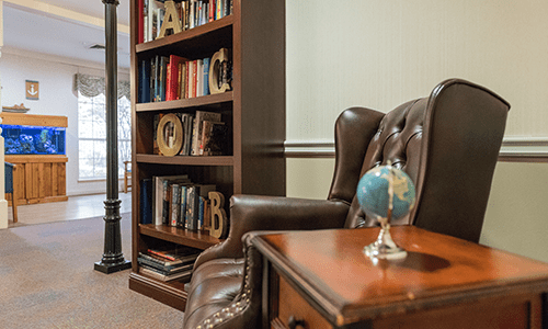 A cozy reading nook with a leather chair, bookshelf, and a small globe on a wooden table.