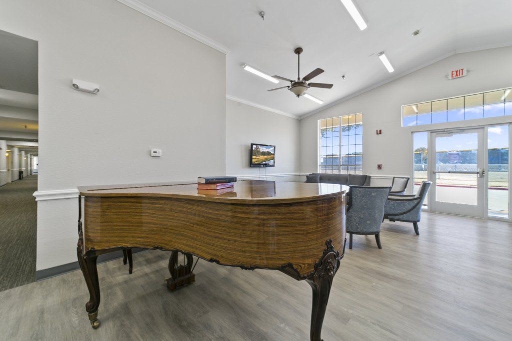 A well-lit room featuring a grand piano, seating area, and large windows.
