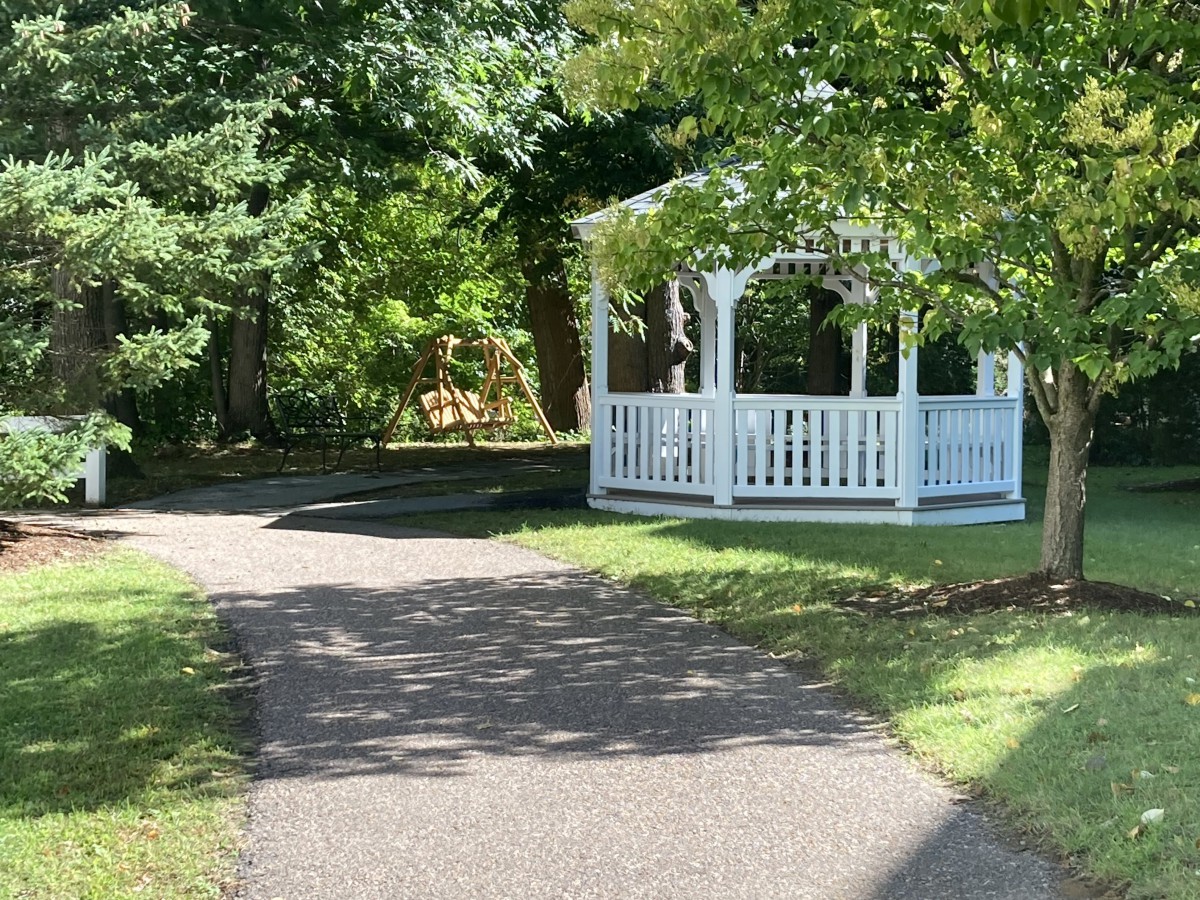 A peaceful outdoor scene featuring a white gazebo surrounded by trees along a winding pathway.