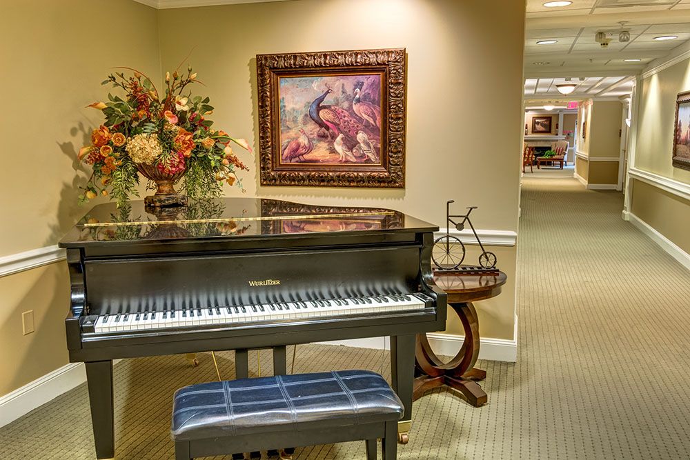 A stylish interior featuring a grand piano with a bench, adorned with artwork and floral arrangements.