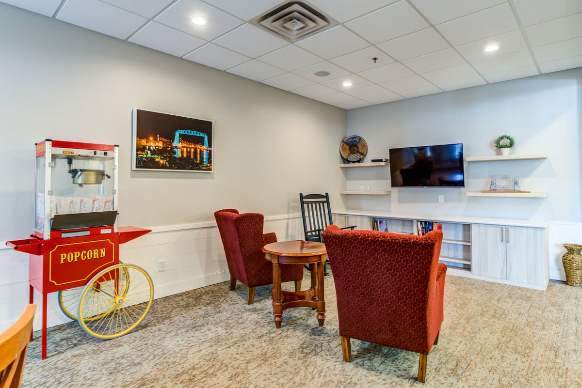 A cozy lounge area with red chairs, a table, a television mounted on the wall, and a popcorn machine.
