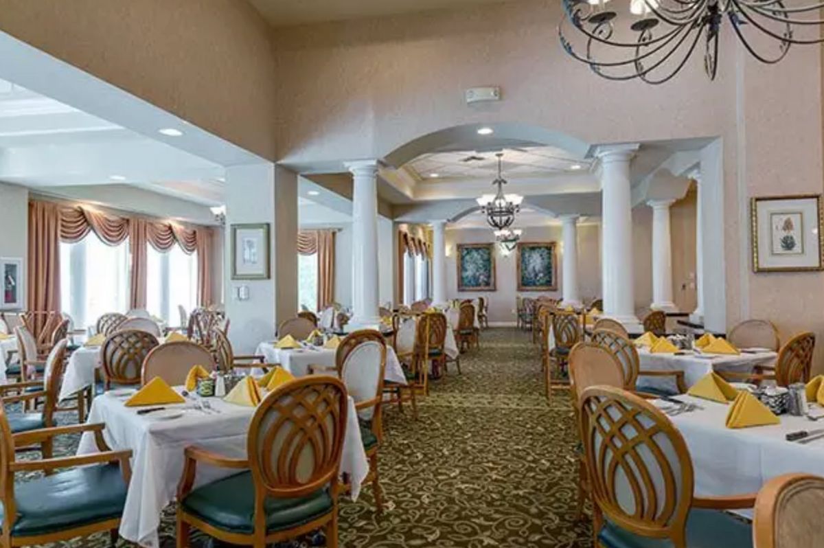 An elegant dining room with neatly arranged tables and chairs, featuring chandeliers and a patterned carpet.