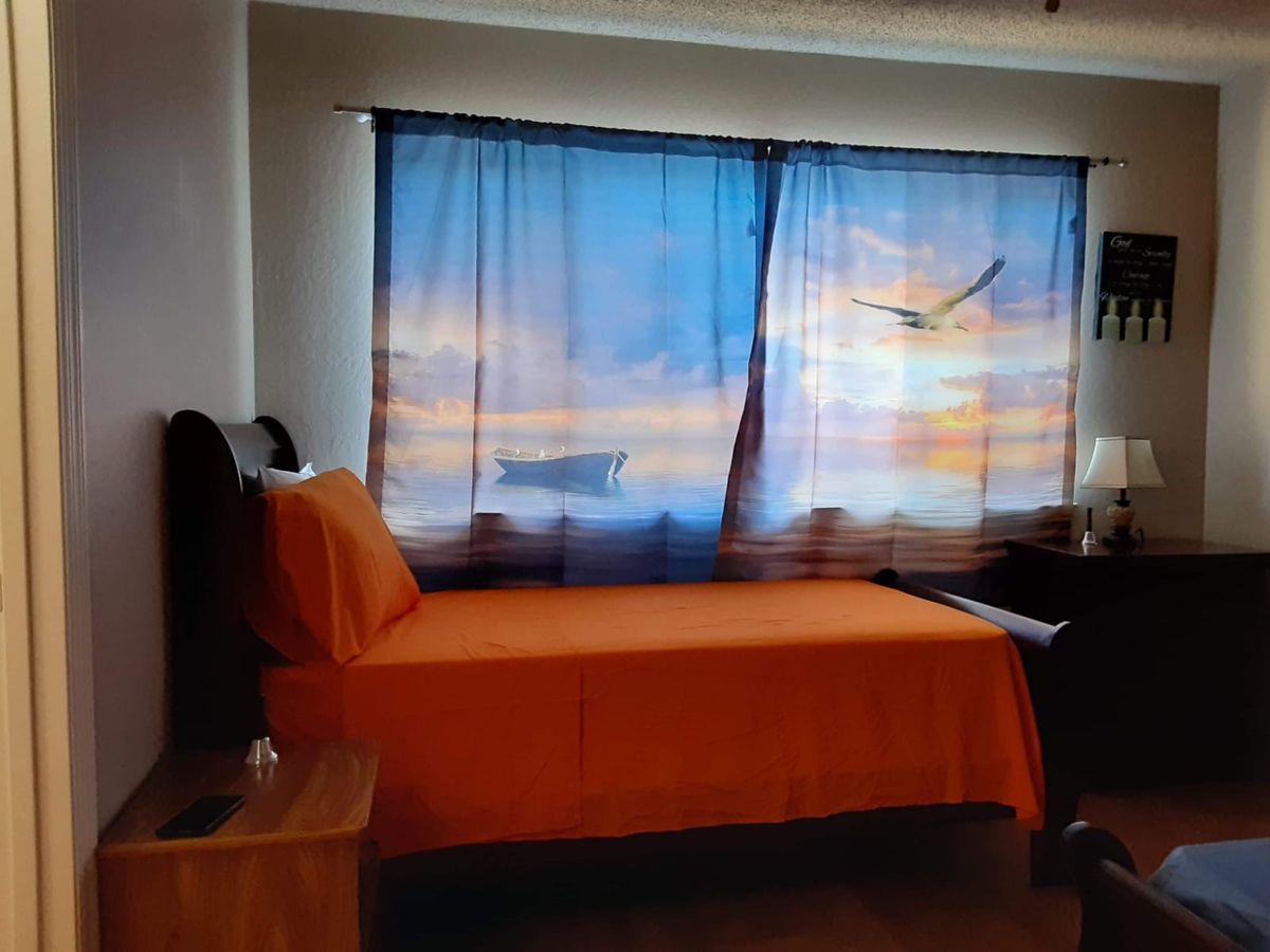 A cozy bedroom with orange bedding and scenic curtains depicting a sunset and bird.