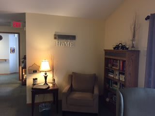 A cozy corner of a living room featuring an armchair, a lamp on a side table, and a bookshelf.