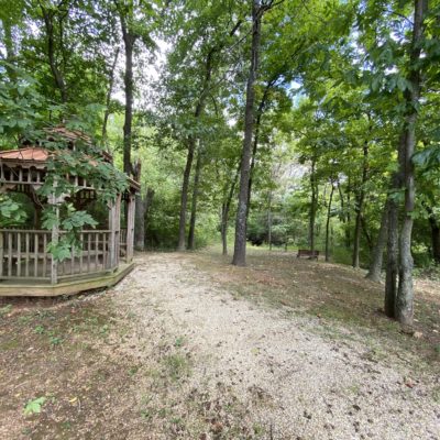 A peaceful forest setting with a gazebo and pathway surrounded by trees.