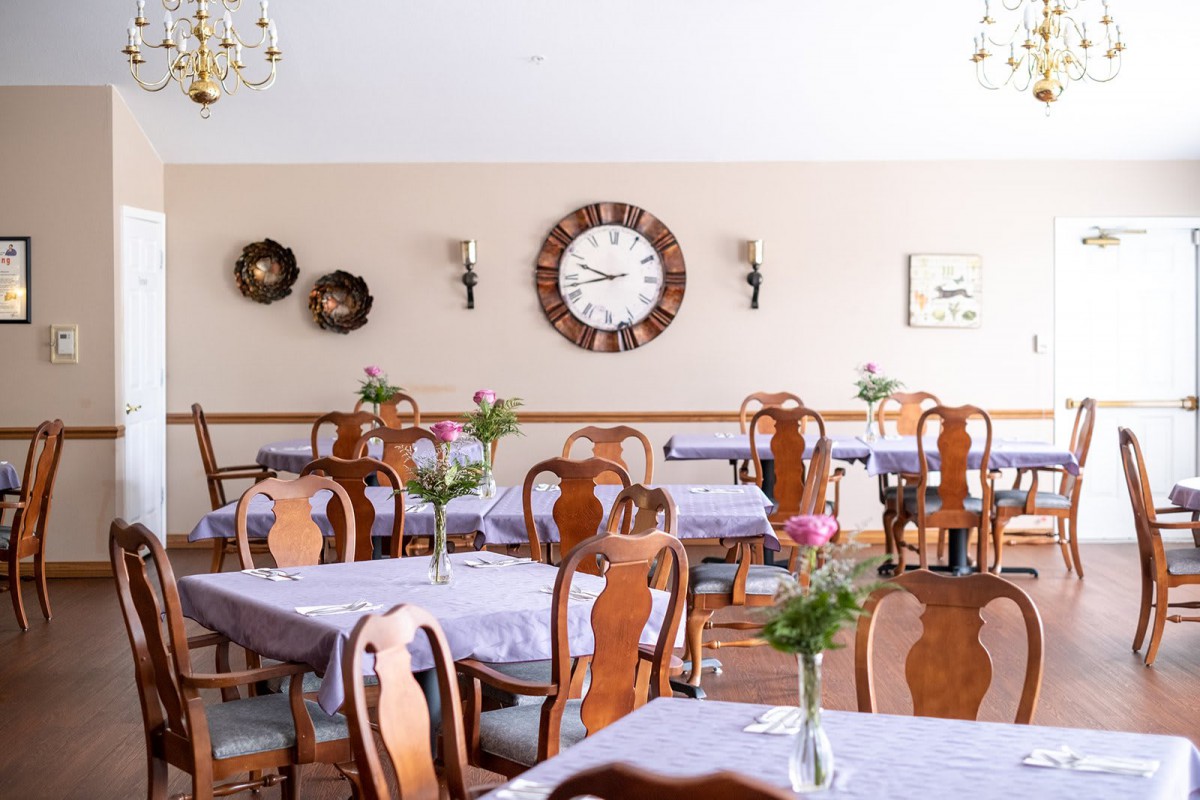 An elegantly set dining area with wooden chairs and tables adorned with fresh flowers.