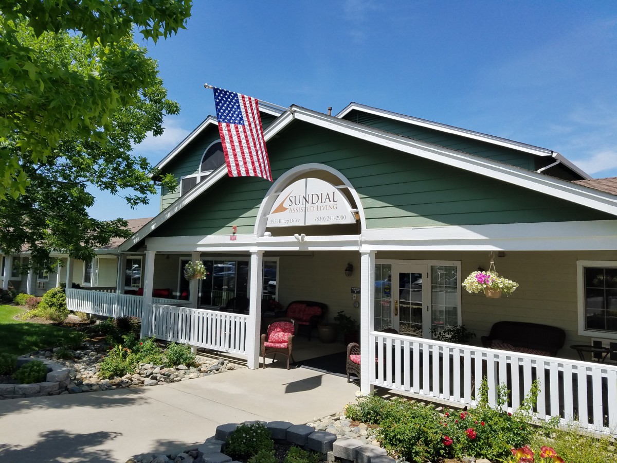 A charming house with a porch and an American flag, surrounded by a well-maintained garden under a clear blue sky.