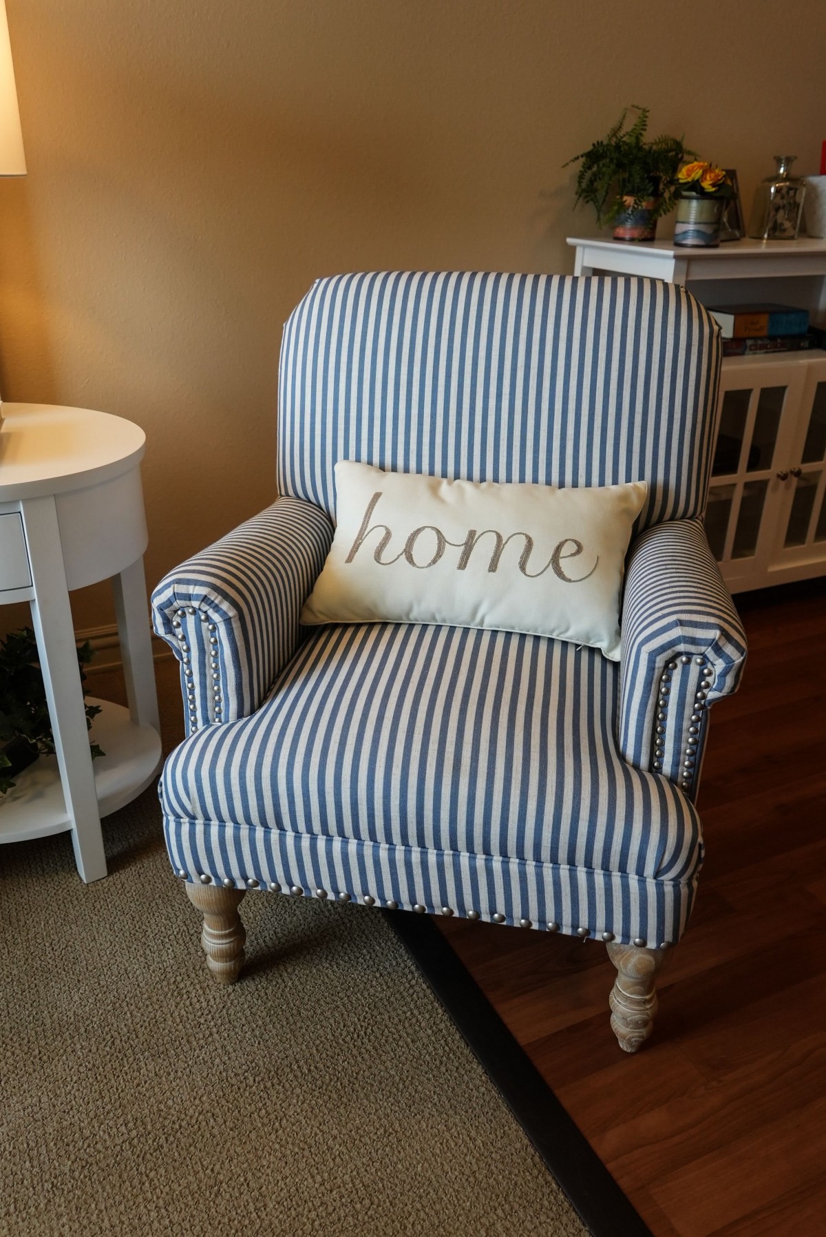 A cozy striped armchair with a decorative 'home' cushion in a warmly lit living room.