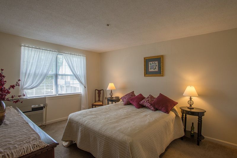 A cozy bedroom with a neatly made bed, warm lighting from two lamps, and a window allowing natural light to filter in.