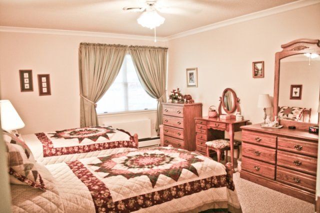 A cozy bedroom featuring two twin beds with quilt covers, vintage wooden furniture including a dresser and vanity table, complemented by elegant curtains.