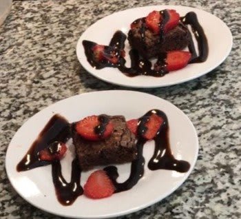 Delicious brownies topped with fresh strawberries and drizzled with chocolate sauce.