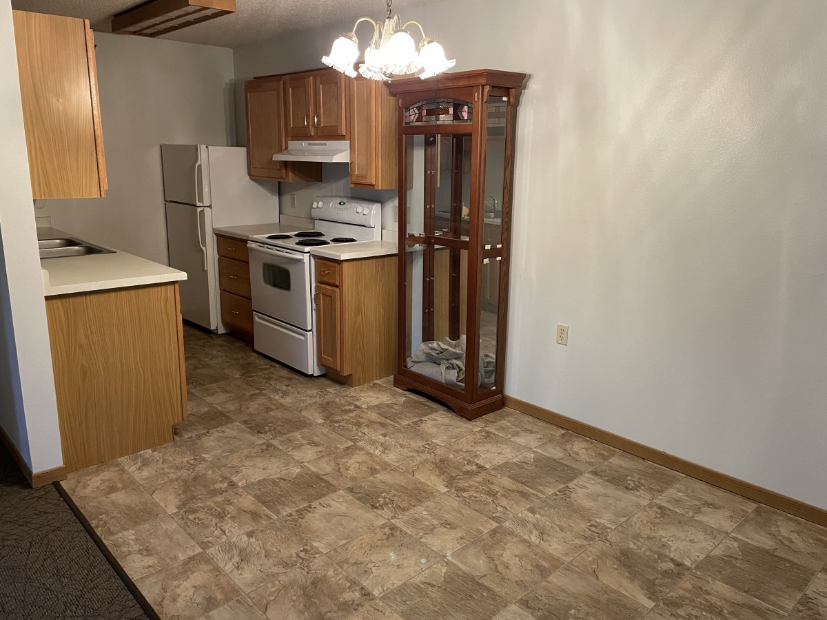 A spacious kitchen with wooden cabinets, a stove, and refrigerator, featuring tile flooring and a china cabinet.