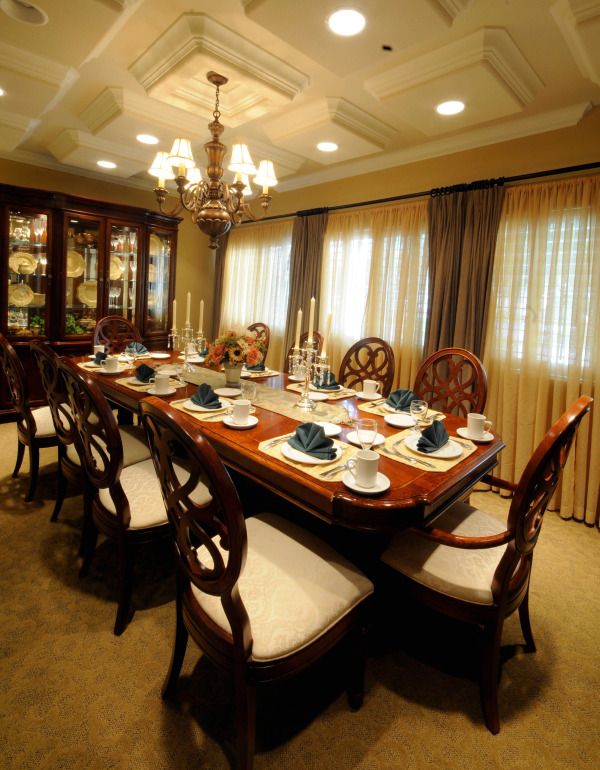 An elegantly set dining room table with a chandelier overhead and curtains in the background.