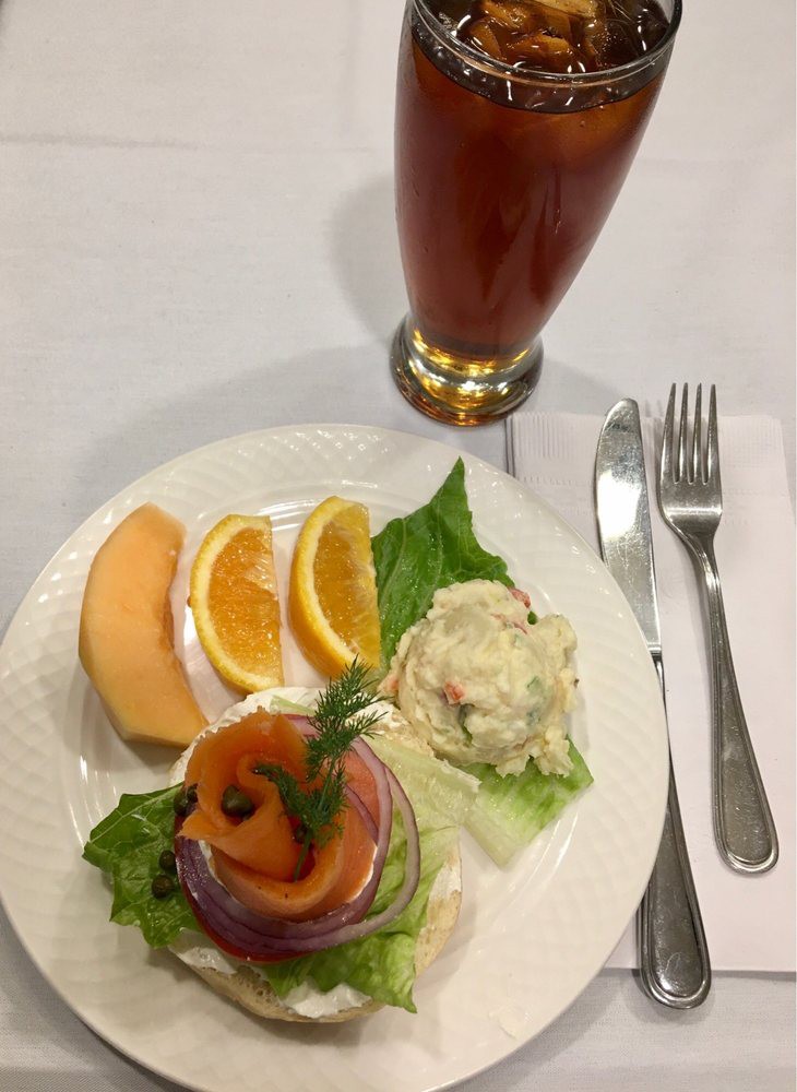 A plate of smoked salmon garnished with greens and served with orange and cantaloupe slices, alongside a glass of iced beverage.