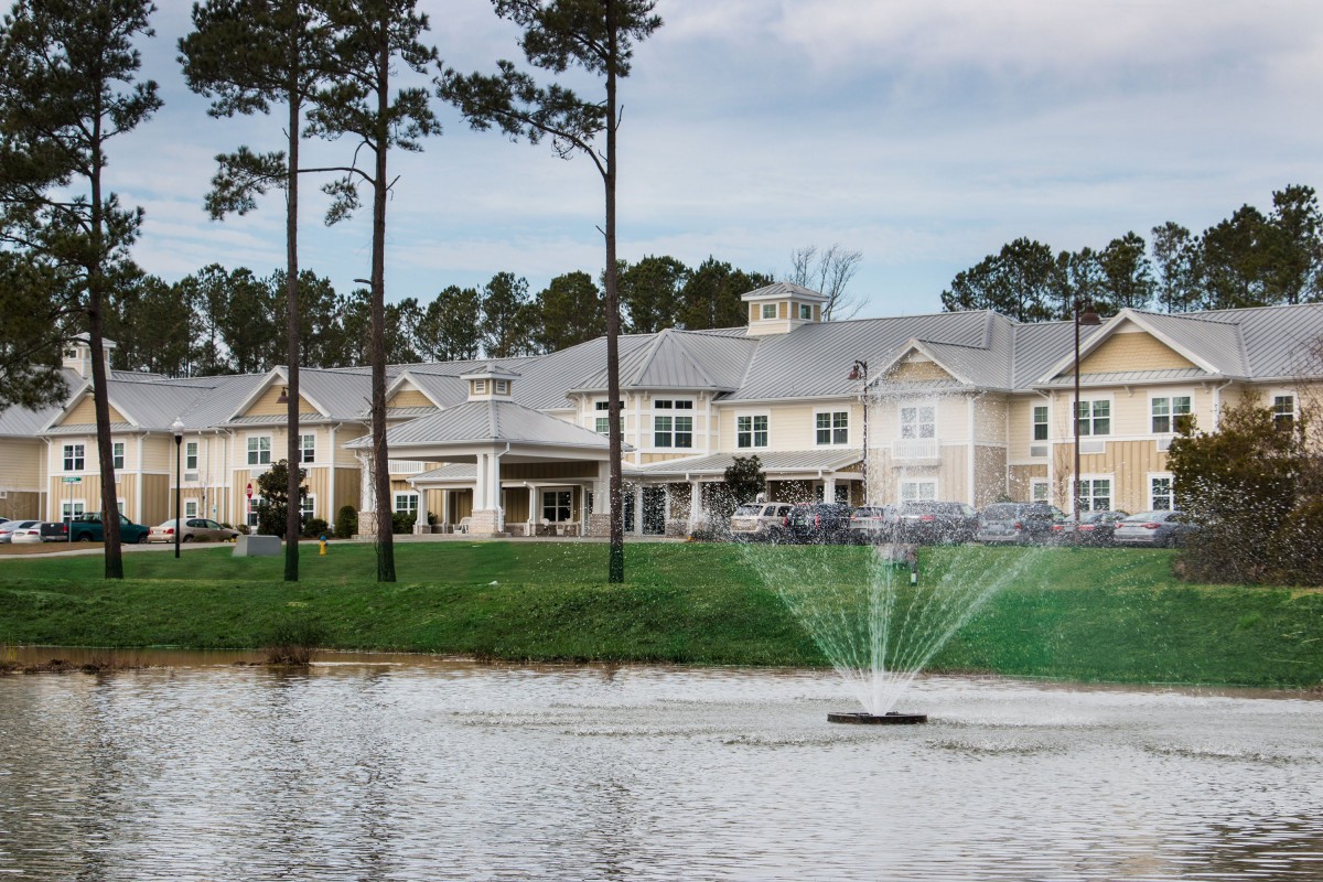 A scenic view of a building by a lake with a fountain and trees.