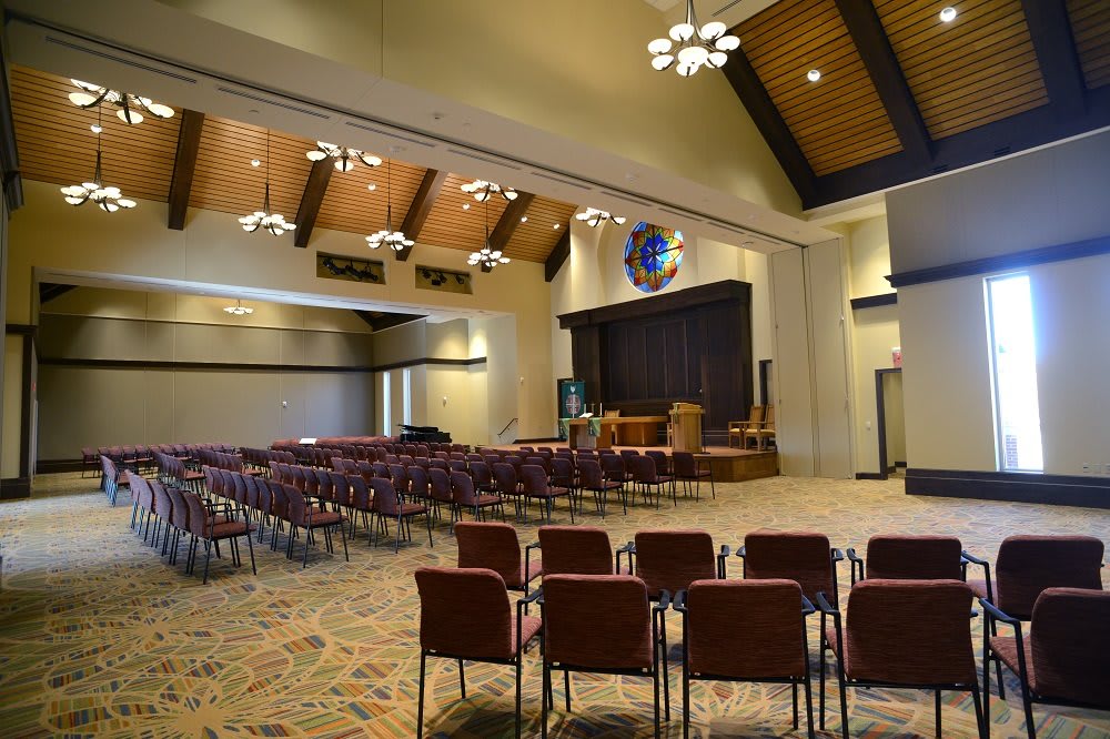 An empty auditorium with rows of chairs facing a stage, featuring elegant lighting and a carpeted floor.