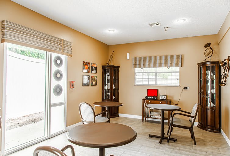 A cozy room with tables, chairs, and decor, featuring natural light from windows.