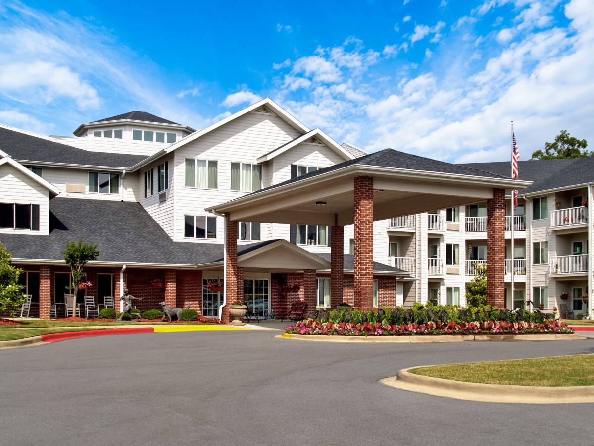 A modern residential building with a landscaped entrance under a clear blue sky.