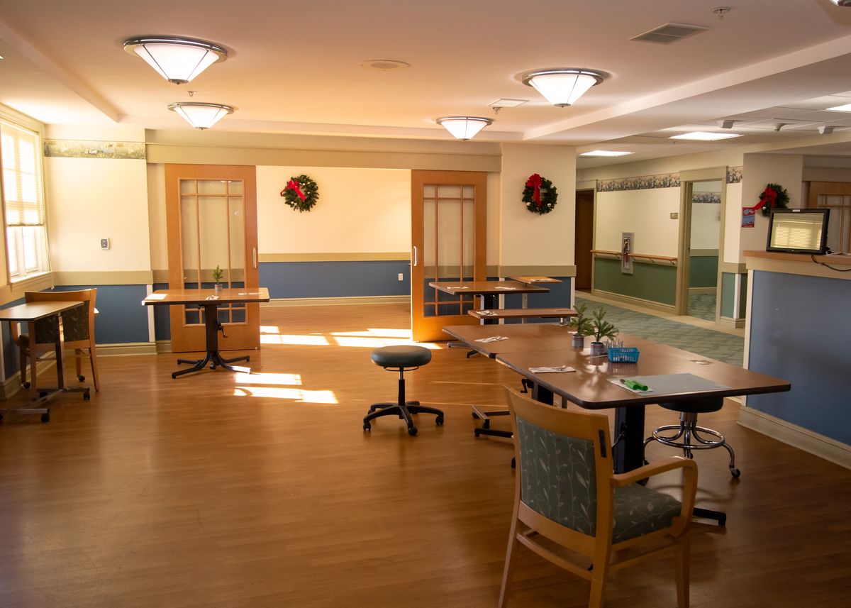 A spacious room with tables and chairs, decorated with wreaths and illuminated by bright ceiling lights.