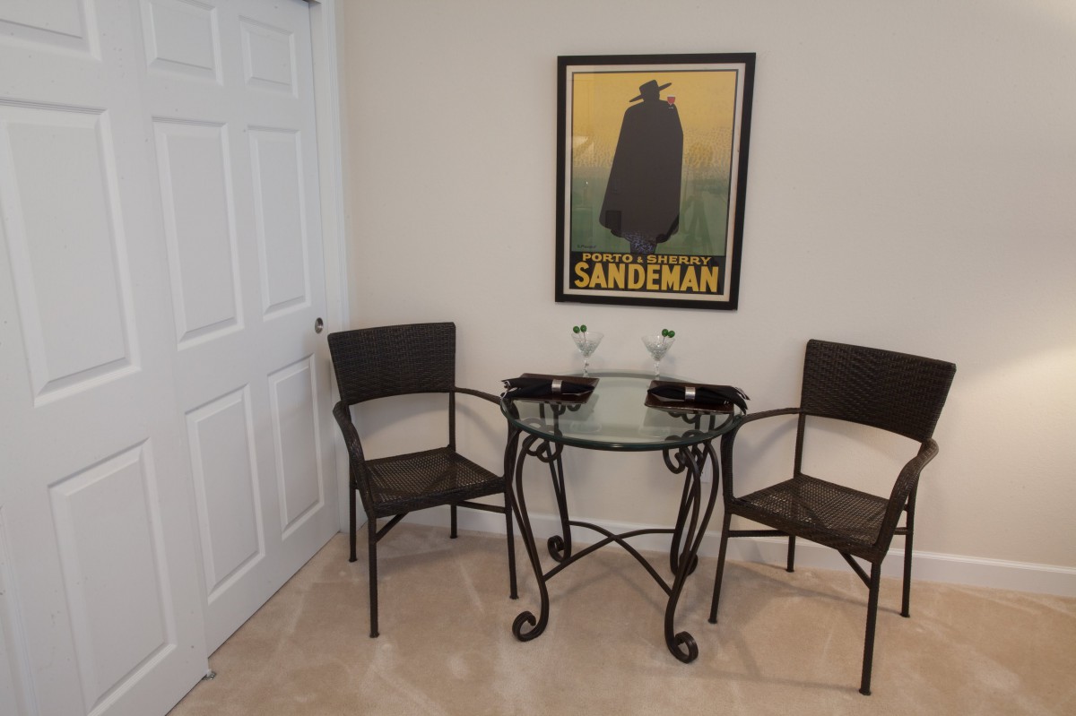 A small dining area with a glass table and two chairs, featuring a poster on the wall.