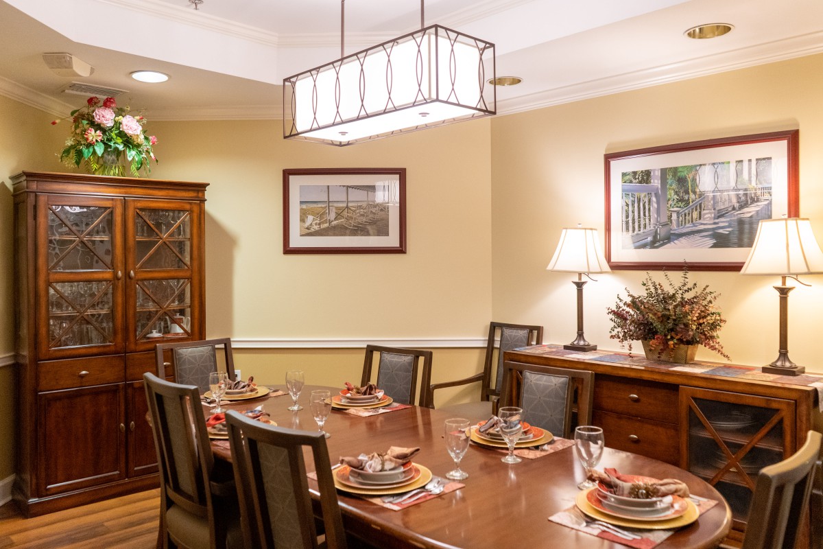 A neatly arranged dining room with a large wooden table, surrounded by chairs, and adorned with elegant decor.