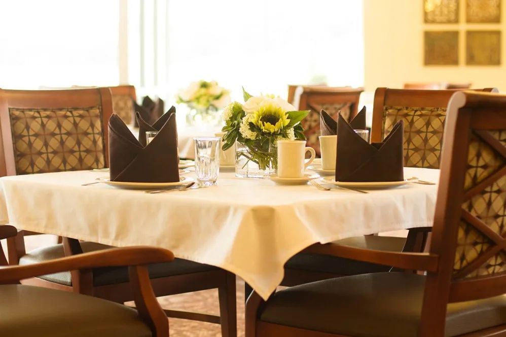 A beautifully set dining table with black napkins folded elegantly and a centerpiece of sunflowers.