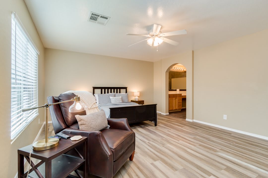A spacious bedroom with modern furnishings, featuring a comfortable bed, leather armchair, and wooden flooring.