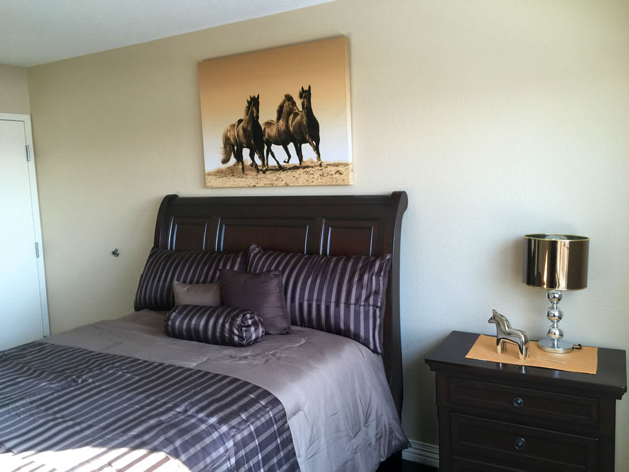 A cozy bedroom featuring a stylish bed with striped bedding and artwork of horses on the wall.