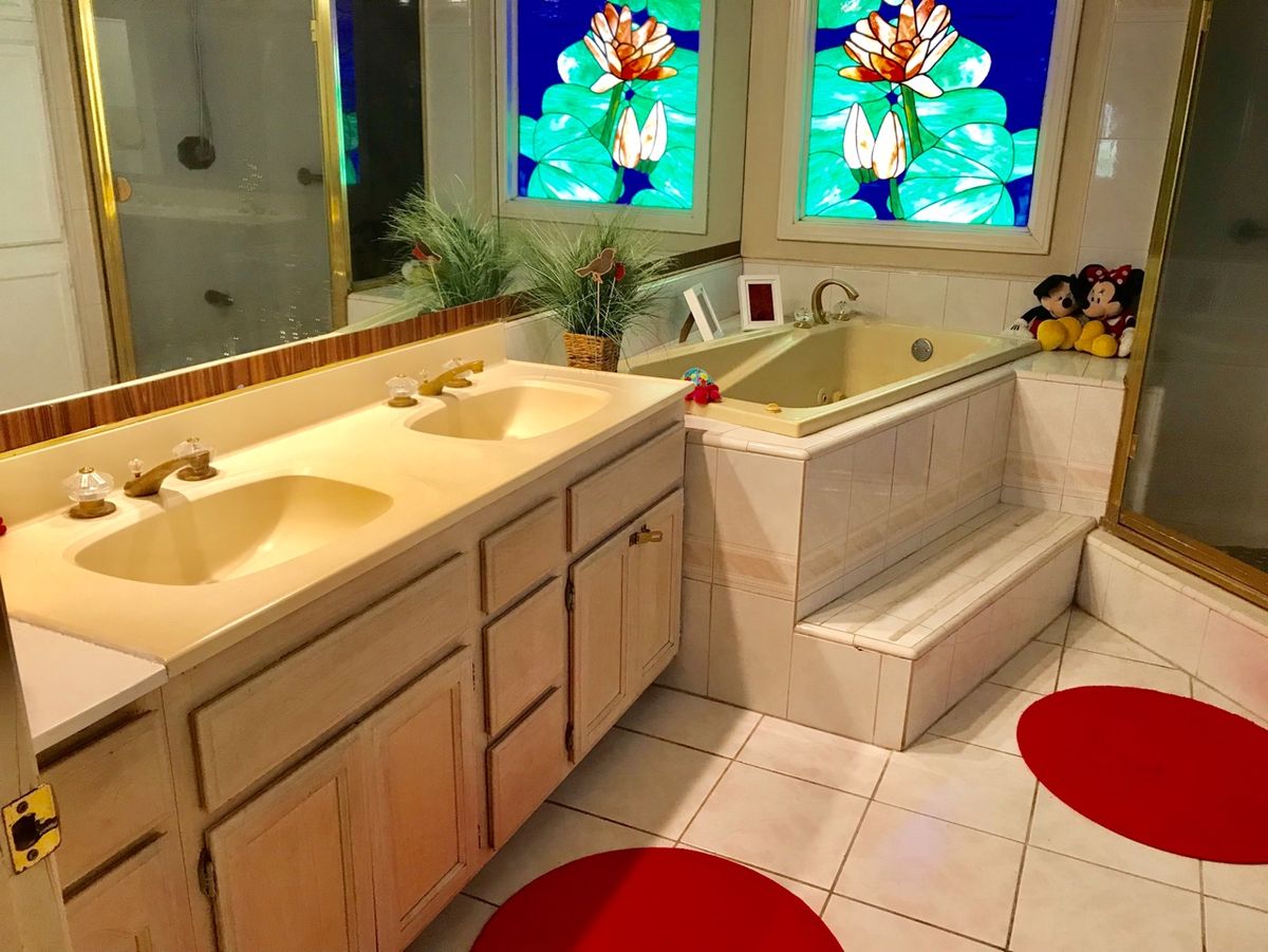 A bright bathroom with double sinks, a bathtub, and decorative stained glass windows.