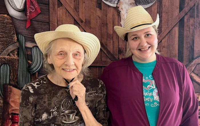 Two women wearing cowboy hats, smiling together indoors.