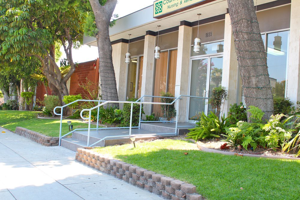 A storefront with a ramp and handrails surrounded by trees and greenery.