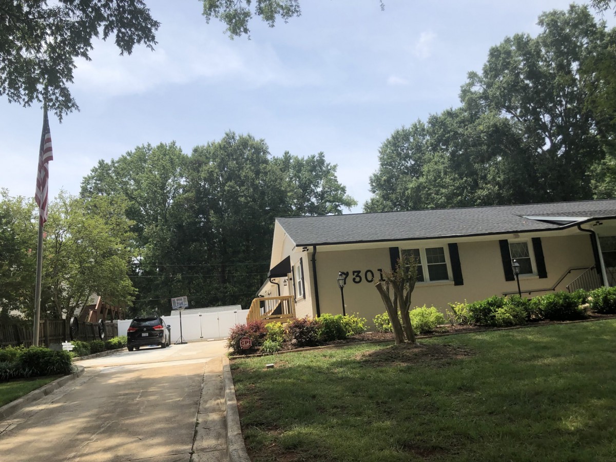 A suburban house with a driveway and a well-maintained lawn surrounded by trees.