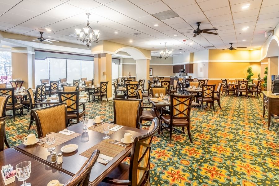 A spacious restaurant interior with neatly arranged tables and chairs, featuring chandeliers and a patterned carpet.