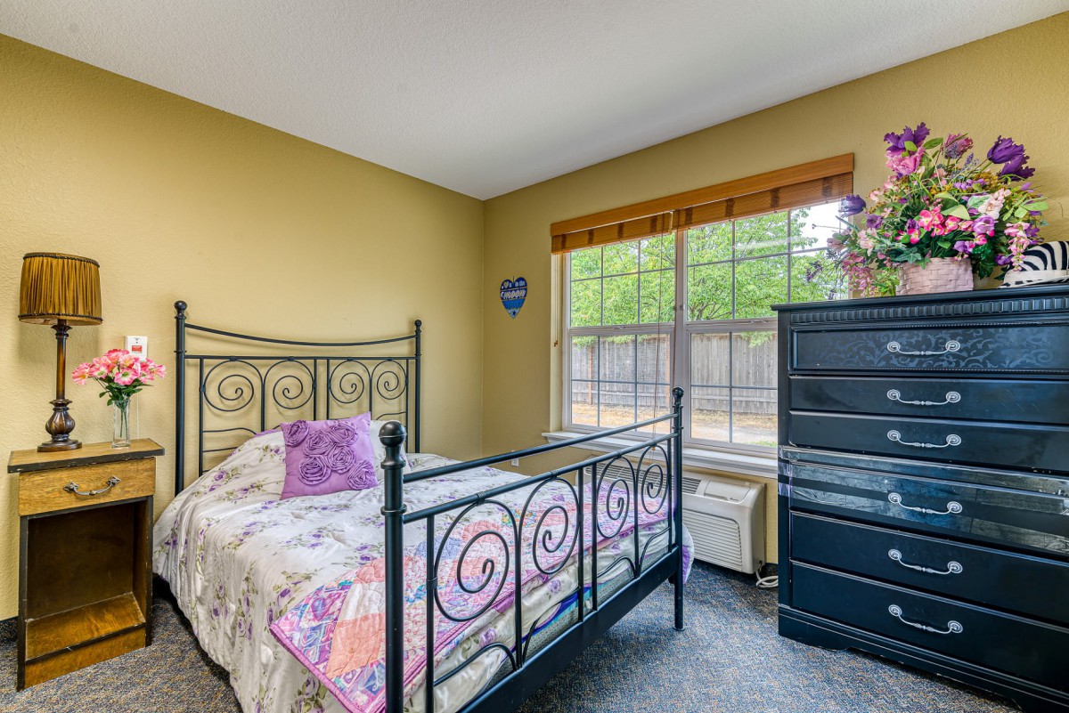 A cozy bedroom with a metal-framed bed, colorful bedding, and a large window letting in natural light.