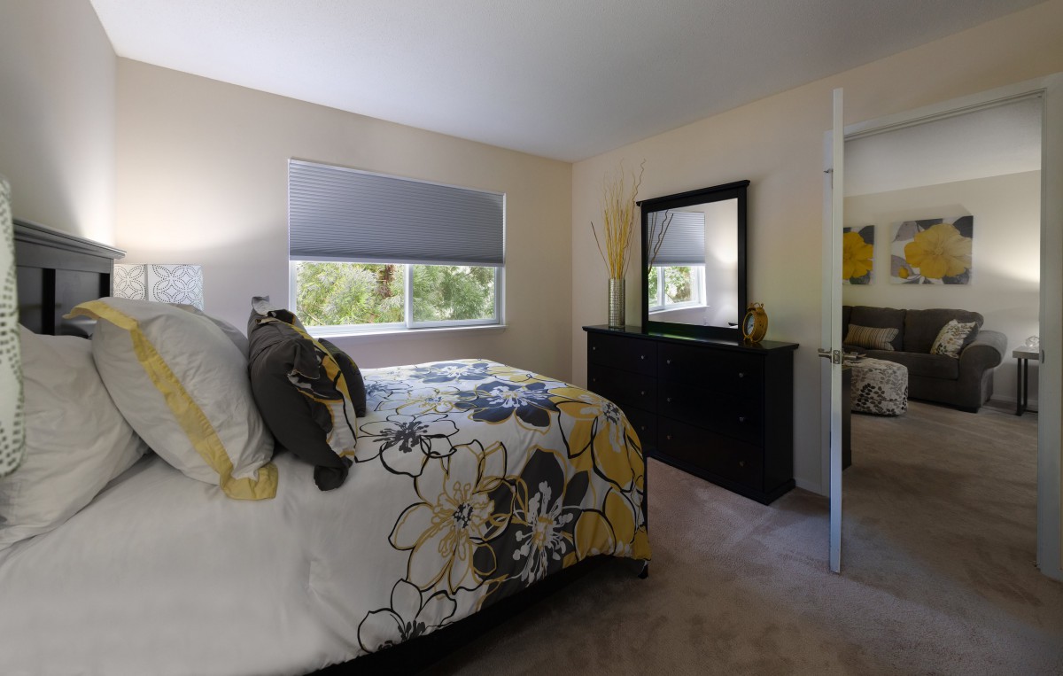 A cozy bedroom featuring a floral bedspread, large mirror, and soft carpeting.