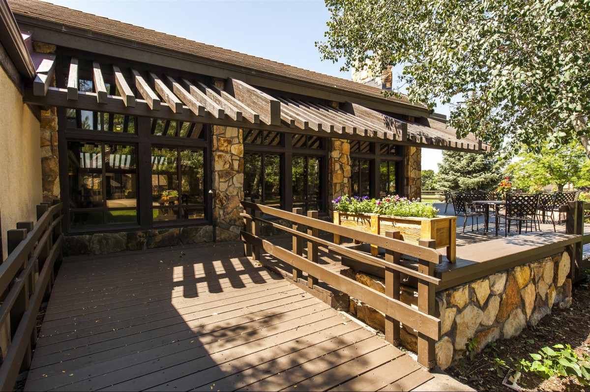 A rustic building with a wooden deck and stone facade surrounded by trees on a sunny day.