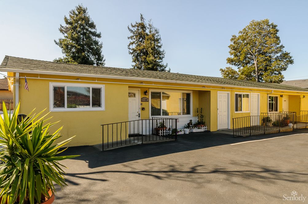 A single-story yellow house with a driveway and trees in the background.