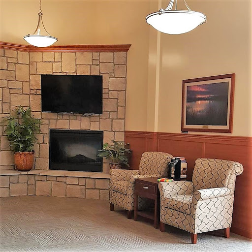 A cozy waiting area featuring comfortable chairs, a TV, and a fireplace, complemented by indoor plants and artwork.