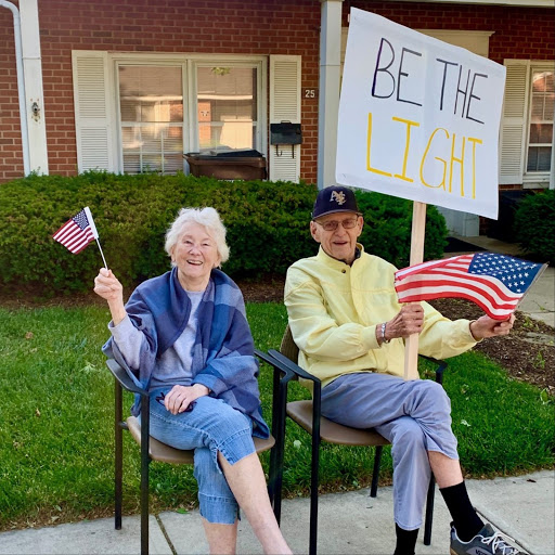 Two cheerful seniors celebrating patriotism with American flags and a motivational sign.