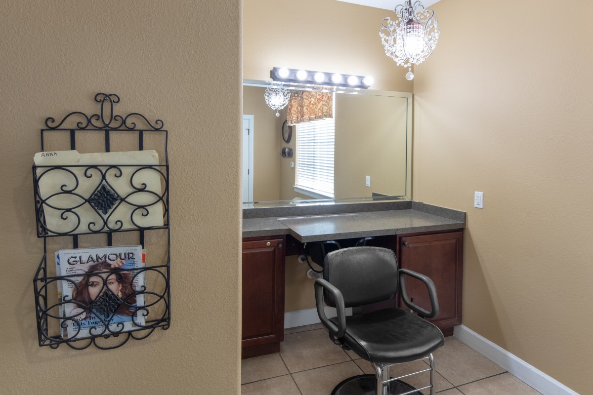 A well-lit hair salon styling area featuring a mirror, a black styling chair, and a chandelier.