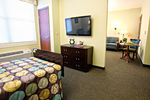 A cozy room featuring a bed with a colorful quilt, a television mounted on the wall, and a dresser, creating a comfortable living space.