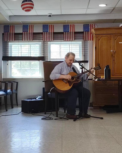 A musician performing on stage with an acoustic guitar, surrounded by flag decor.