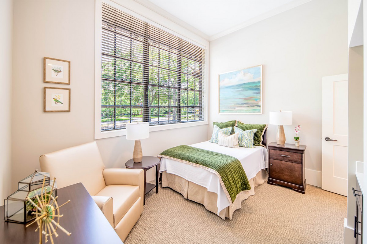 A bright and cozy bedroom with large windows, decorated with green accents and a scenic artwork.